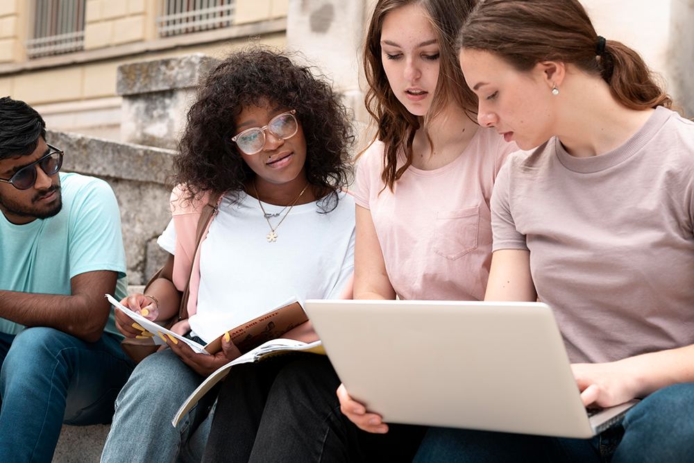 Jovens estudantes de diferentes etnias compartilhando conhecimento enquanto olham para a tela de um Notebook.