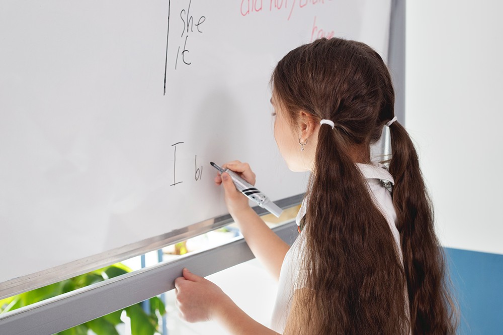 Menina em sala de aula escrevendo em inglês em uma lousa branca.