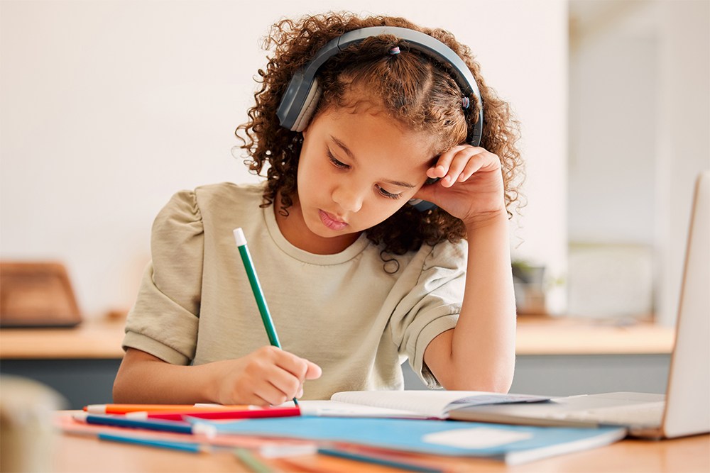 Menina usando fones de ouvido para estudar enquanto escreve em um caderno